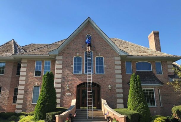 Professional window washer on a ladder cleaning a brick home — the benefits of clean windows start outside