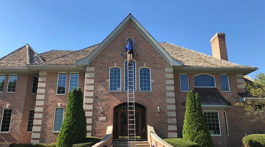 Professional window washer on a ladder cleaning a brick home — the benefits of clean windows start outside